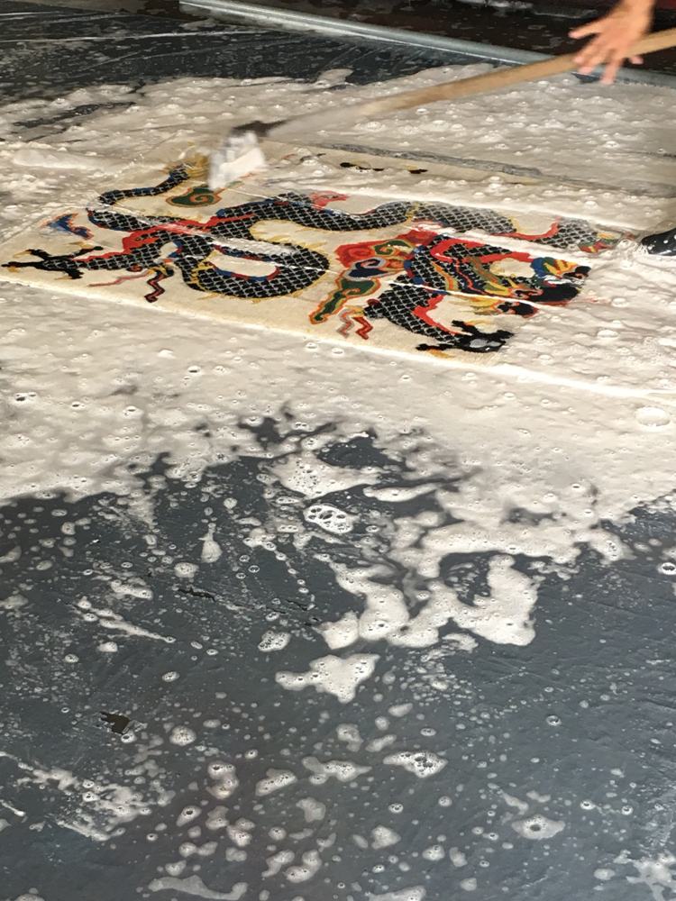Hand washing a dragon-pattern rug with soap and a brush