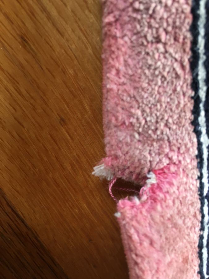 Moth damage eaten through the edge of a pink rug