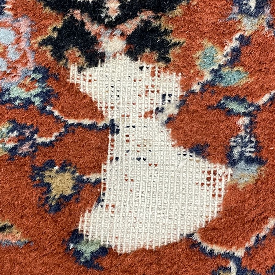 Rust-red Persian-design rug with a hole worn down to the foundation